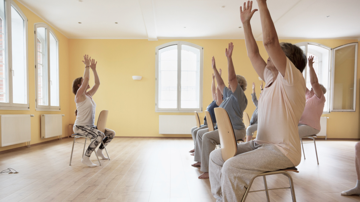 Photo of people practicing chair yoga with hands in air